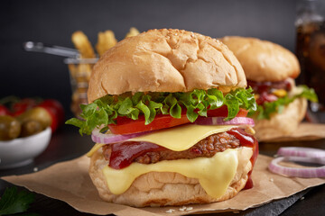 Two mouth-watering, Homemade hamburger with fresh vegetables and cheese lettuce and mayonnaise served, French fries on pieces of brown paper on black stone table . concept of fast food and junk food