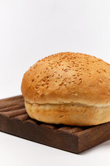 white bun with sesame seeds on the edge of a kitchen board on a white background