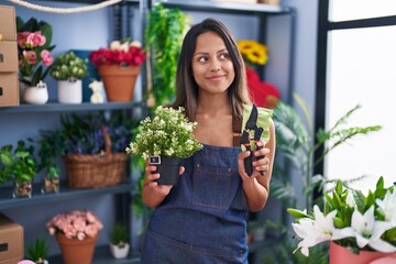 Hispanic young woman working at florist shop smiling looking to the side and staring away thinking.