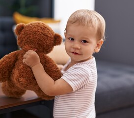 Adorable toddler smiling confident playing with teddy bear at home