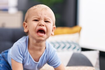 Adorable toddler sitting on sofa crying at home