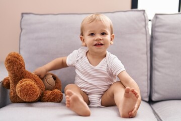 Adorable toddler playing with teddy bear sitting on sofa at home