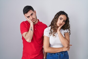 Young hispanic couple standing over isolated background thinking looking tired and bored with depression problems with crossed arms.