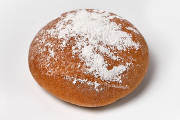 round bun sprinkled with powdered sugar on a white background close view