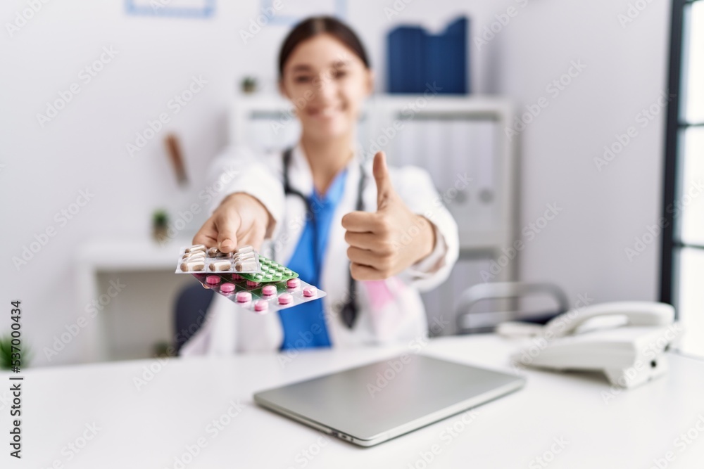 Sticker young hispanic doctor woman wearing doctor uniform holding prescription pills at clinic smiling happ