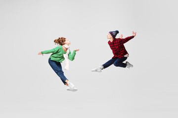 Creative portrait of ballet dancers in warm clothes and hats dancing, having fun isolated on gray...