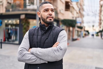 Naklejka premium Young latin man standing with arms crossed gesture at street