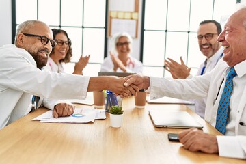 Group of middle age doctor smiling and clapping to partners handshake in a medical meeting at the...