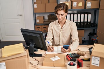 Young caucasian man ecommerce business worker using smartphone writing on notebook at office