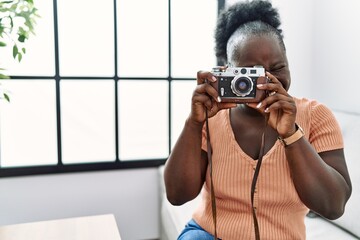 Young african american woman using vintage camera sitting on sofa at home