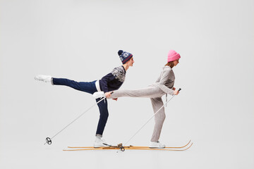 Weekend activities.Two funny retro skiers in warm winter casual wear skiing isolated on grey...