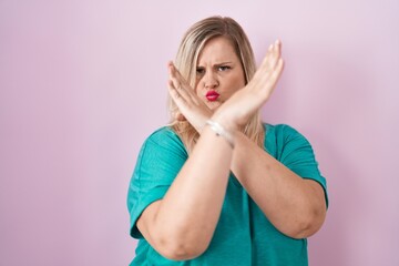 Caucasian plus size woman standing over pink background rejection expression crossing arms doing negative sign, angry face