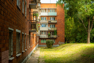 Old brick residential building in Eastern Europe. Poor area surrounded by trees. Small partially destroyed balconies with trash