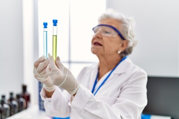 Senior grey-haired woman wearing scientist uniform holding test tubes at laboratory