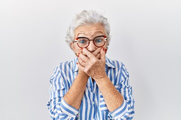 Senior woman with grey hair standing over white background shocked covering mouth with hands for...