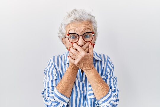 Senior woman with grey hair standing over white background shocked covering mouth with hands for mistake. secret concept.