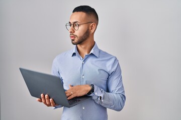 Young hispanic man working using computer laptop looking to side, relax profile pose with natural face and confident smile.