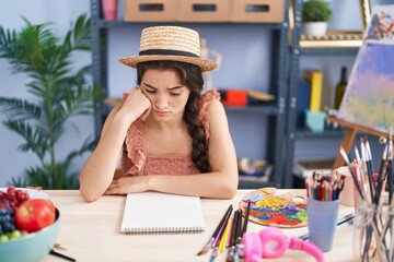 Young hispanic woman artist sitting with sad expression at art studio