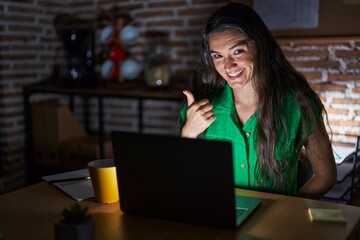 Young teenager girl working at the office at night doing happy thumbs up gesture with hand. approving expression looking at the camera showing success.