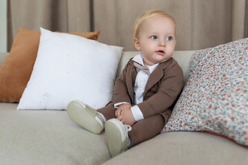 stylish baby in business clothes sits on the couch and looks to the right