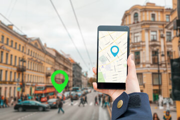 A woman's hand holds a smartphone with an online map app.In the background is a blurred city street with a location icon. Concept of online navigation and modern technologies