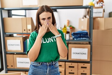 Young brunette woman wearing volunteer t shirt at donations stand laughing and embarrassed giggle...