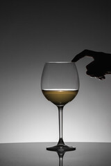 Woman posing her finger on the rim of the glass of white wine. Black silhouette.