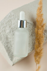 Essential oil or serum and dry pampas herbs on a natural white podium. Frosted bottle with a pipette on a beige background