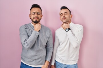 Homosexual couple standing over pink background touching painful neck, sore throat for flu, clod and infection