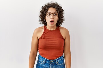 Young hispanic woman wearing glasses standing over isolated background afraid and shocked with surprise and amazed expression, fear and excited face.