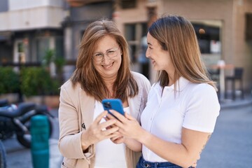 Mother and daughter using smartphone standing together at street