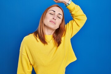 Young woman standing over blue background stretching back, tired and relaxed, sleepy and yawning...
