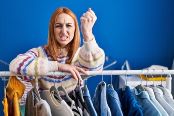 Young woman searching clothes on clothing rack annoyed and frustrated shouting with anger, yelling crazy with anger and hand raised