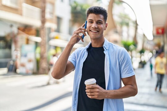 Young hispanic man talking on the smartphone drinking coffee at street