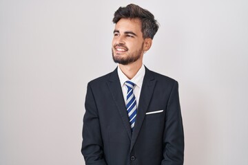 Young hispanic man with tattoos wearing business suit and tie looking away to side with smile on face, natural expression. laughing confident.