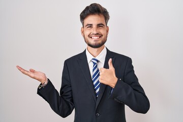 Young hispanic man with tattoos wearing business suit and tie showing palm hand and doing ok gesture with thumbs up, smiling happy and cheerful