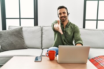 Young hispanic man with beard wearing call center agent headset working from home smiling friendly...