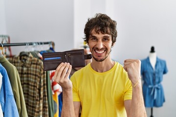 Young hispanic man holding leather wallet at retail shop screaming proud, celebrating victory and...