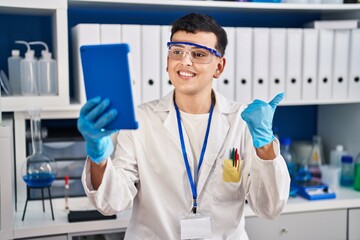 Non binary person working at scientist laboratory using tablet pointing thumb up to the side smiling happy with open mouth