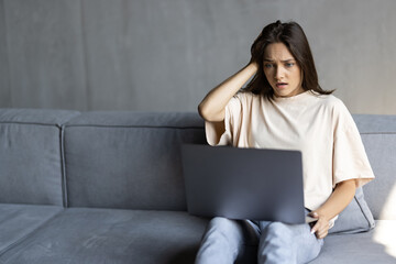 Stressed young woman looking at laptop screen, touching forehead, reading bad news in email