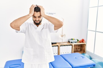 Obraz premium Young handsome man with beard working at pain recovery clinic suffering from headache desperate and stressed because pain and migraine. hands on head.