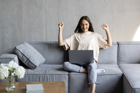 Young woman sit on couch at home triumph receive pleasant email or read good news on laptop onlin