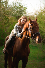 Fototapeta premium Woman with long hair posing with a brown horse in a forest in a sunny meadow.
