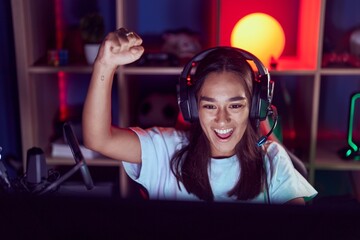 Young beautiful hispanic woman streamer playing video game with winner expression at gaming room