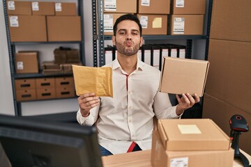 Young hispanic man with beard working at small business ecommerce holding delivery packages looking...