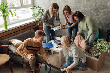 Smiling, energetic, busy friends packing luggage and trying to fit things in suitcase in living room, show out, move in