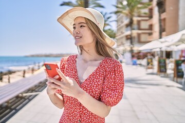 Young chinese girl wearing summer hat using smartphone at the promenade.