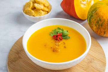 Autumn pumpkin cream soup with pumpkin spices. Delicious and bright vegetarian dish with foodstyling of fresh parsley with hot pepper and seasonings on a white background.  Menu concept, copy space