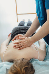 Male masseur with strong hands professionally massaging scapulas and shoulders. Beautiful naked young woman with perfect skin getting back massage at spa salon.