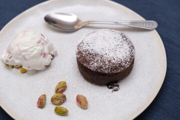Brown chocolate soufflé with ice cream and pistachios decoration on a plate with spoon